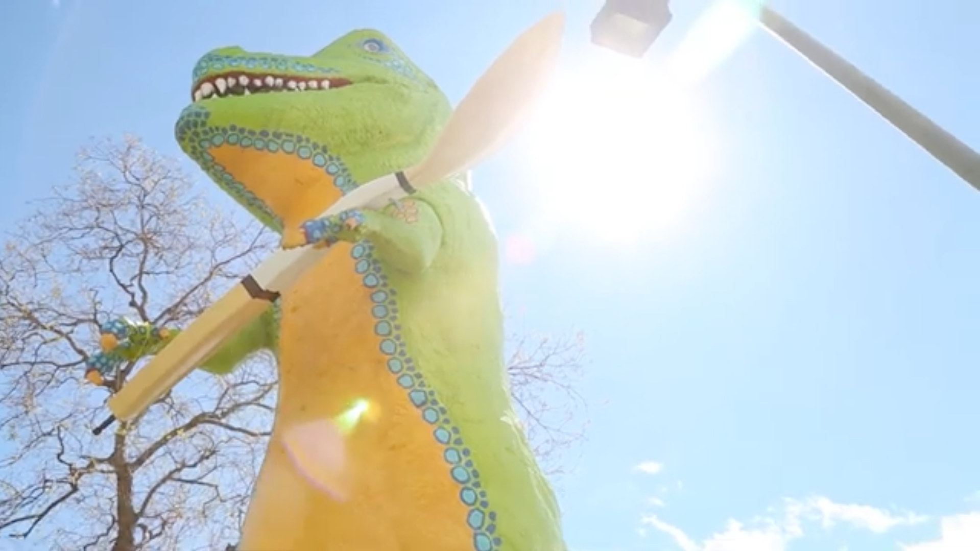 Large colorful dinosaur sculpture prop against a bright blue sky