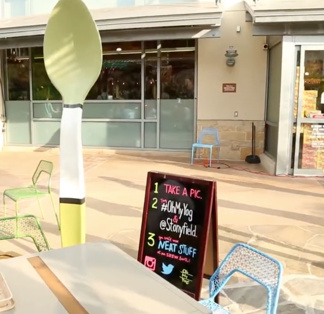 Oversized green spoon prop at an outdoor SXSW brand activation with colorful chairs